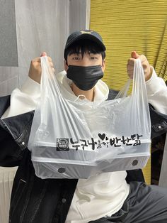 a man wearing a face mask and holding up a plastic bag with japanese writing on it