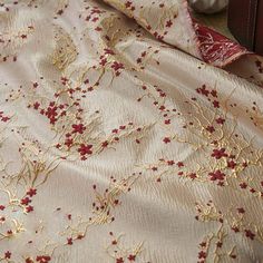 a red and gold floral design on a white fabric with metallic threading, next to a brown leather case