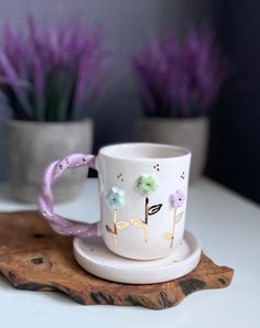 a white coffee cup sitting on top of a wooden tray next to purple flowers in vases