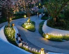 two people sitting on benches in the middle of a park at night with lit up trees and bushes