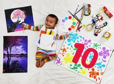 a baby is laying on the ground with some art supplies around him and there are paintings