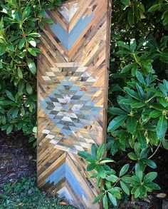 a wooden sculpture sitting in the grass next to some bushes and trees with green leaves on it