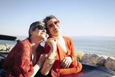 two women sitting in the back of a pick up truck looking out at the ocean