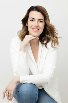 a woman in white jacket and jeans sitting on the ground with her hand under her chin