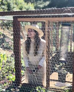 a woman in a white dress and hat standing behind a chicken wire fence with a birdcage