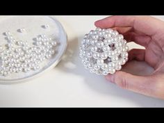 a hand holding a bead ball next to a bowl with pearls on the surface