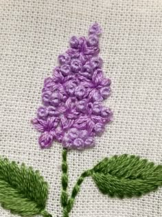 a close up of a purple flower on a white cloth with green leaves and thread