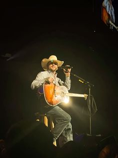 a man wearing a cowboy hat and holding a guitar in front of a microphone on stage