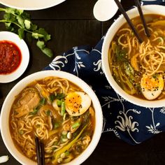 two bowls of soup with noodles and an egg in the middle, on a table