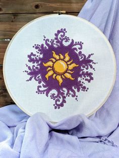 a purple and yellow cross stitched sun on a white hoop