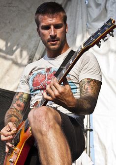 a man with tattoos on his arm playing an electric guitar in front of a tent