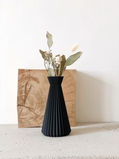 a black vase with white flowers in it on a table next to a wooden block