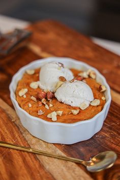 two scoops of ice cream sit in a bowl on a wooden cutting board next to a spoon