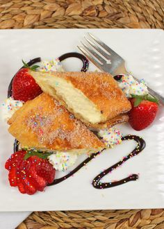 a white plate topped with two desserts and strawberries next to a knife and fork