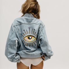 the back of a woman's jean jacket with an eye painted on it