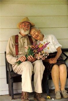 an old couple sitting on a bench with flowers