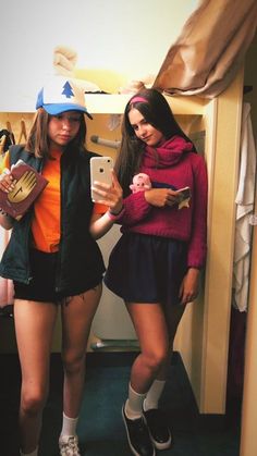 two young women standing next to each other in front of a mirror holding cell phones