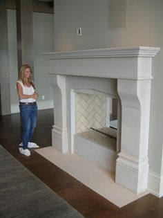 a woman standing next to a fireplace in a living room with hardwood floors and white walls