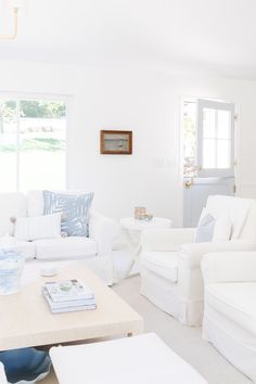 a living room filled with white furniture next to a table and windows in the background