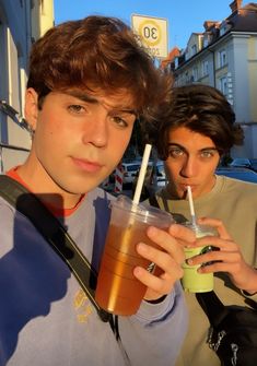 two young men standing next to each other holding drinks