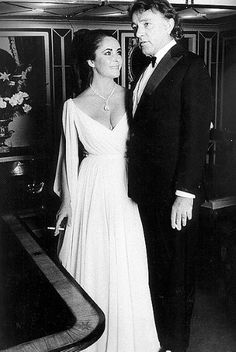 a man and woman standing next to each other in front of a table with flowers on it