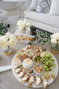 a table topped with cheeses, crackers and grapes next to white roses in vases