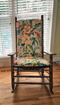 a wooden rocking chair in front of a window with flowers on the seat and back