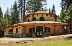 a round building sitting on top of a lush green field next to tall pine trees