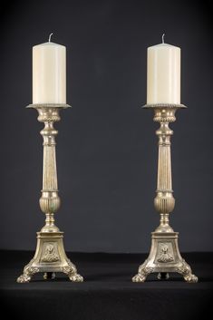 two silver candlesticks sitting next to each other on a black surface with one candle lit