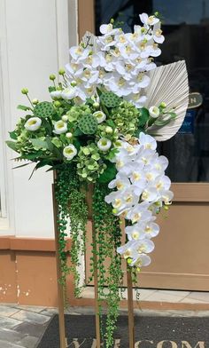 a tall vase with white flowers and greenery in front of a storefront door