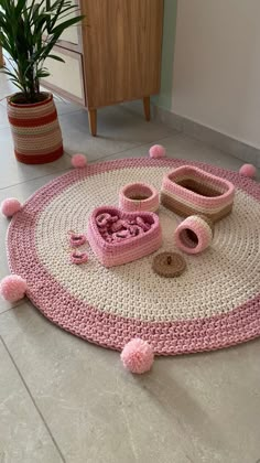 a crocheted rug with pink pom - poms on the floor next to a potted plant