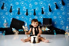 a little boy sitting on the floor with a cake in front of him and some decorations behind him