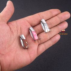 a person is holding three small pieces of silver and pink jewelry in their hand,