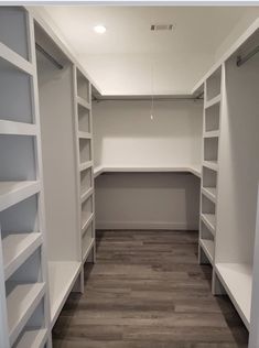 an empty walk in closet with white shelving and wood flooring on the walls