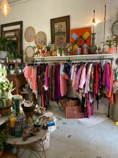 a room filled with lots of clothes hanging on a rack next to a table and potted plants