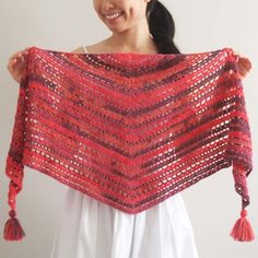 a woman holding up a crocheted shawl with tassels