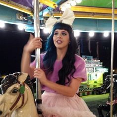 a girl in a pink dress riding on a carousel with a white horse behind her