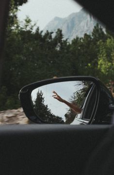 a man's reflection in the side view mirror of a car with trees and mountains in the background