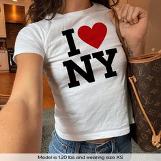 "I Love NY New York" Graphic Slogan Printed On Aesthetic Retro Vintage 90s Y2k Baby Tee Shirt with our own unique font.  🎨 Available in White, Light Pink, Light Blue, Navy, Black. If you need a different color, please let us know! (Ash, Red, Sport Grey & Green)  🎁 Our baby tees are perfect gift for her or him offering timeless fashion and versatility that anyone will cherish. Baby tees, popular in the '90s, have short sleeves and a slightly cropped body, giving a flattering feminine shape. The I Love New York Shirt Outfit Aesthetic, I Heart Ny Shirt, I Love New York Shirt, Baby Tee Shirts, Baby Tees Y2k, Streetwear Mode, Y2k Baby Tee, Vintage Streetwear, I Love Ny