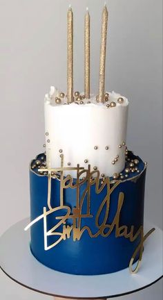 a blue and white birthday cake with gold candles on it's top that says happy birthday