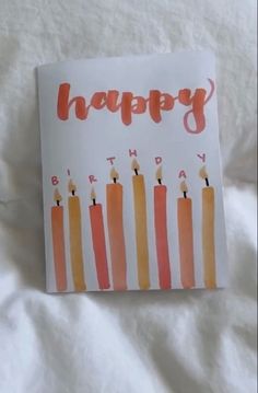 a happy birthday card with candles on it sitting on top of a white bed sheet