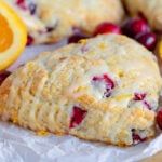 cranberry orange scones with icing sitting on wax paper next to sliced oranges