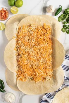 tortillas topped with shredded cheese and limes on a white surface next to other ingredients