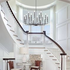 a white staircase with chandelier and two chairs