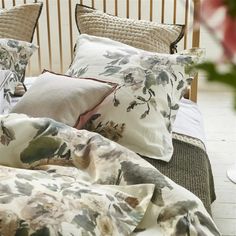 a bed covered in pillows and blankets with flowers on them, next to a plant