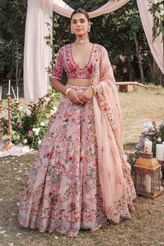 a woman standing in front of an arch with flowers on it wearing a pink lehenga