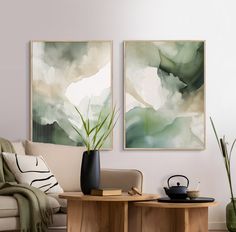 two paintings hang on the wall next to a table with a teapot and potted plant