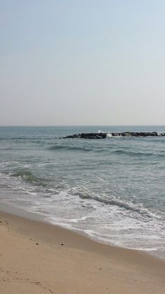 a person walking on the beach with an umbrella in hand and waves coming in to shore