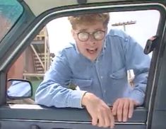 a man with glasses is sticking his head out the window of a truck and making a face