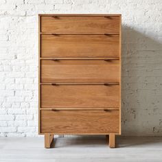 a wooden chest of drawers in front of a white brick wall and wood flooring